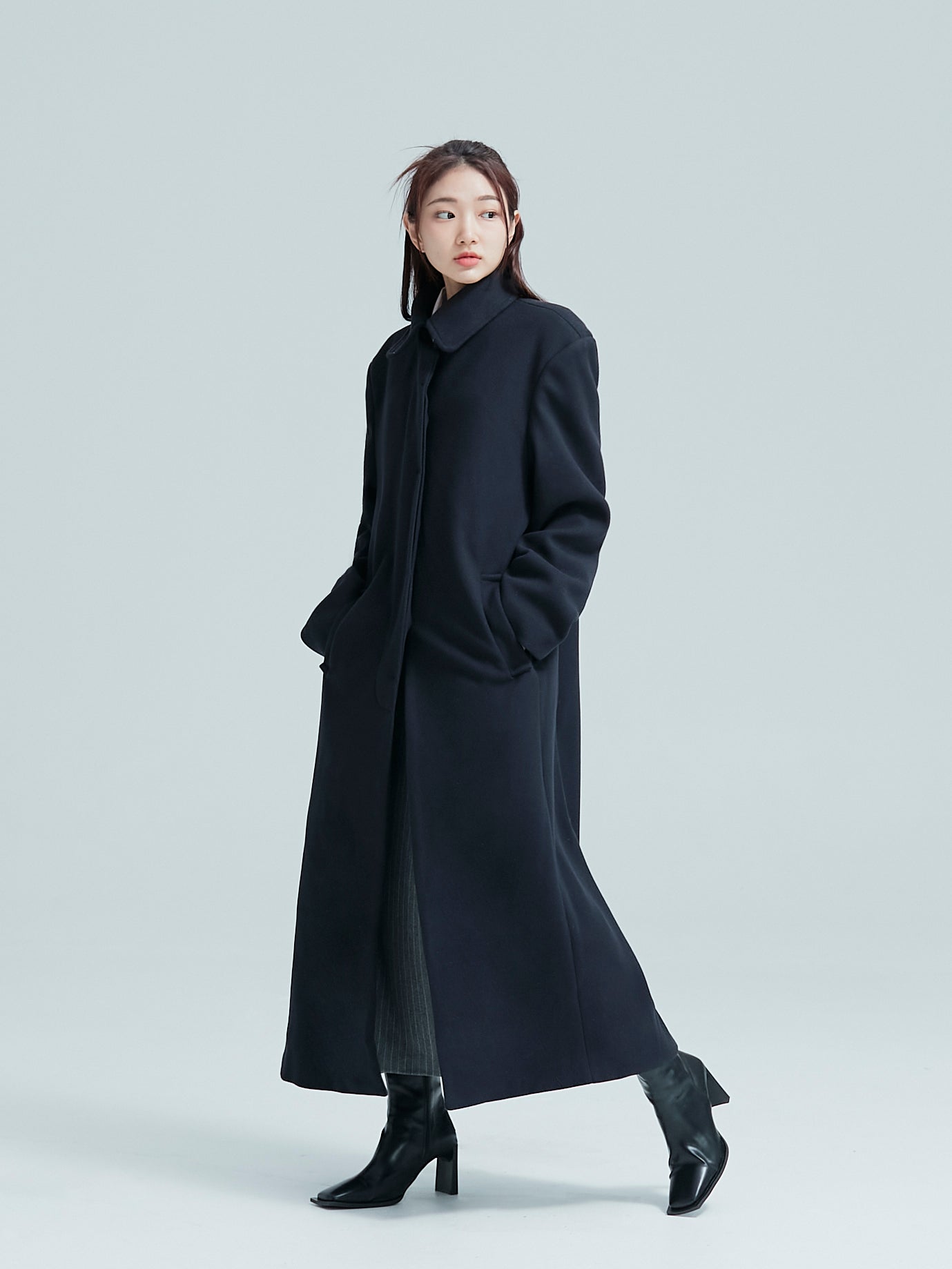 A side angle of the model posing while wearing the single breasted overcoat.