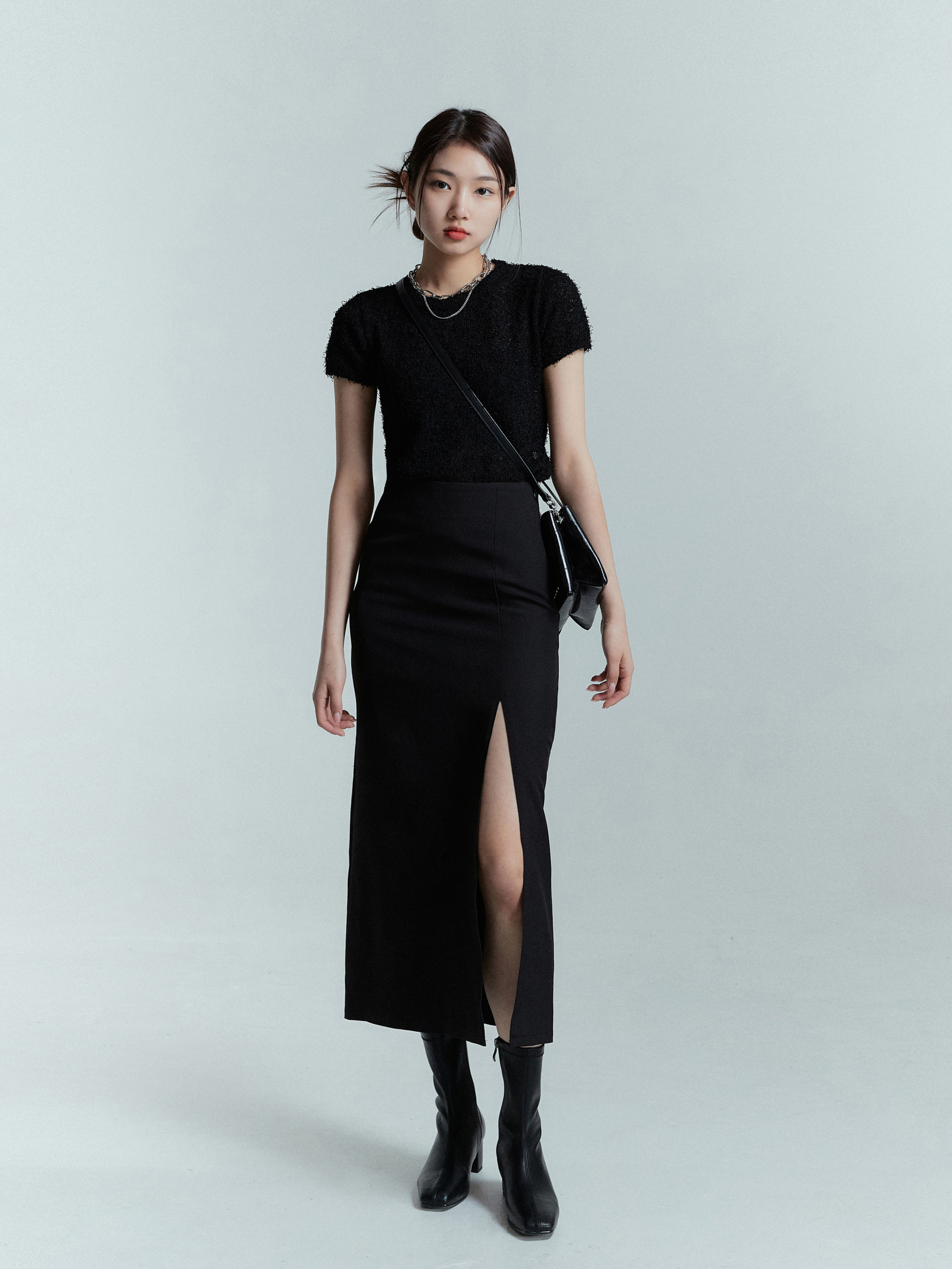 The model stands tall as she pairs the black slit midi skirt with a black fuzzy knit top, effortlessly showcasing a chic and stylish ensemble.