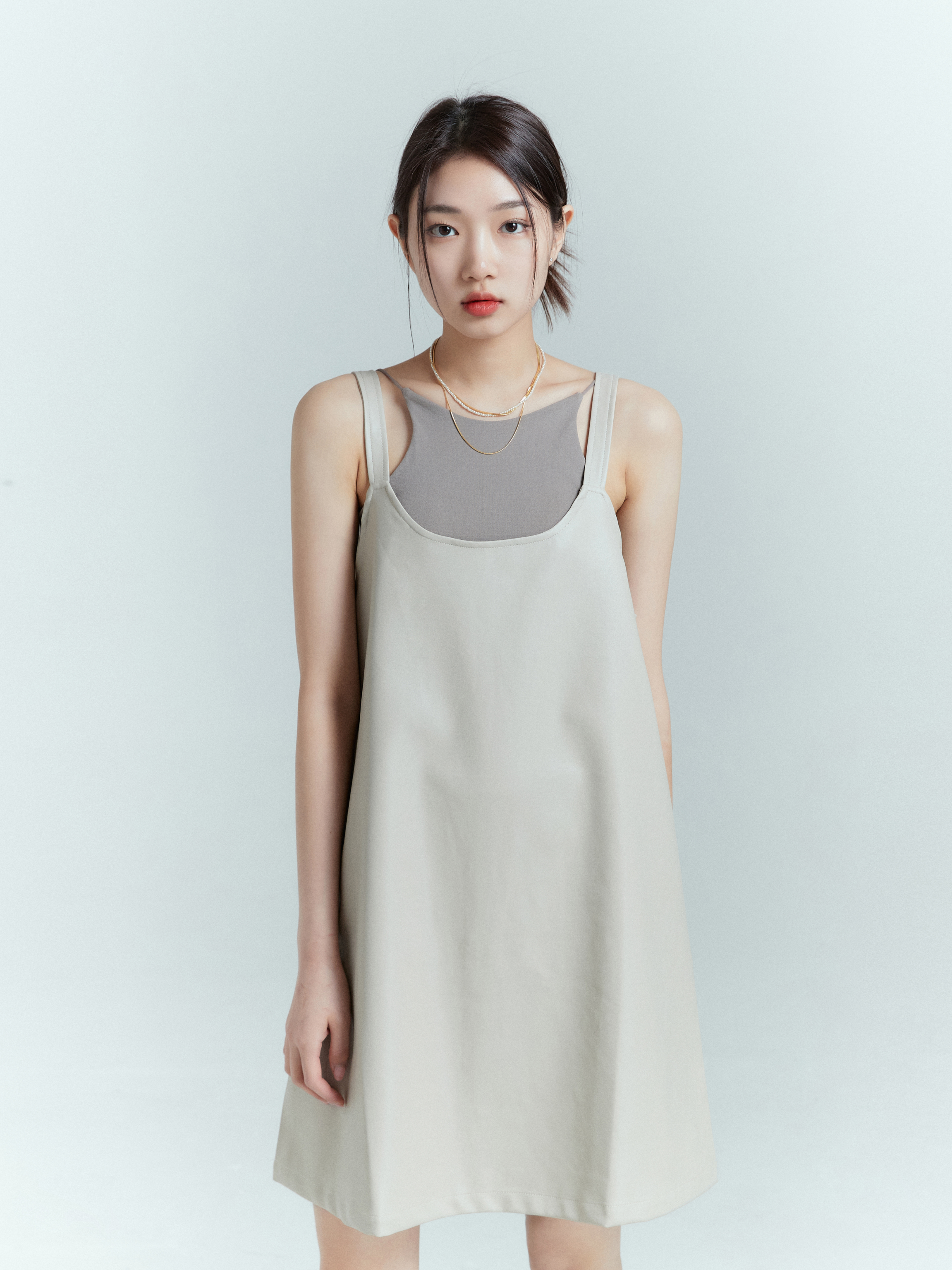 Front view of the model in contemporary fashion, wearing the spaghetti strap tank matched with the light beige tank dress.