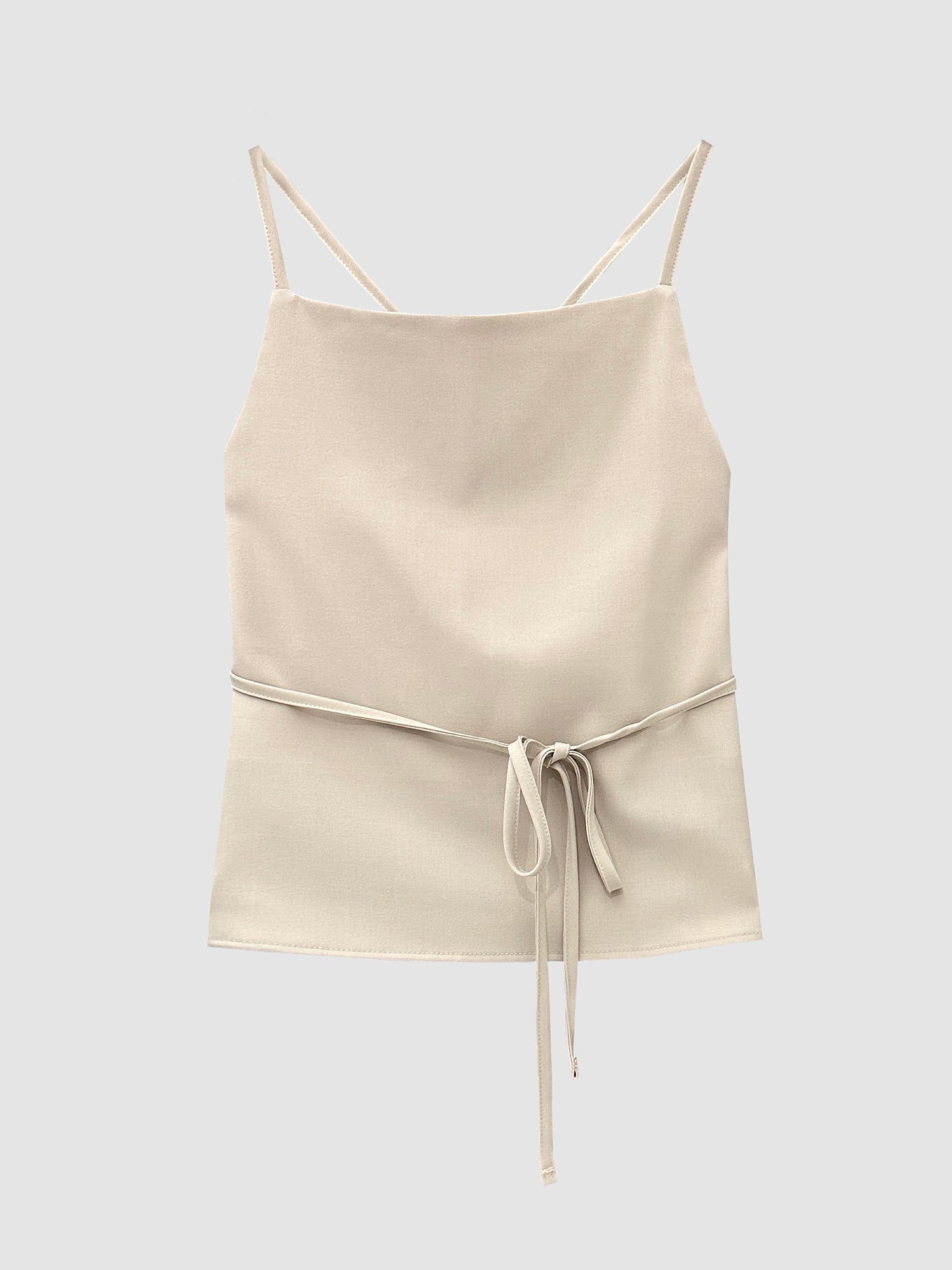 Front detailed shot of the cream strappy top showcasing its strap around the waist and front detailed designs.