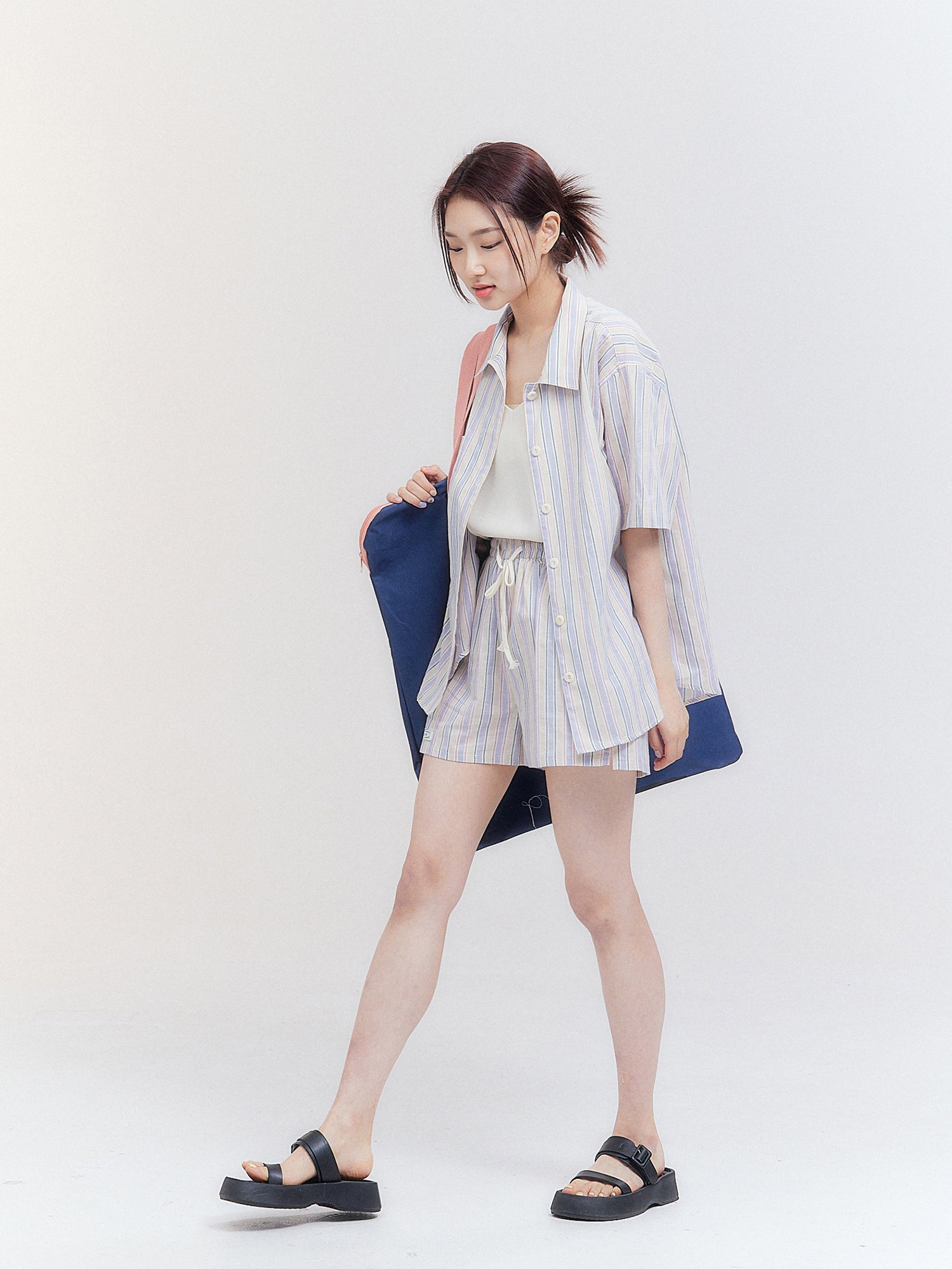 Experience the dynamic energy of Korean street fashion as the model gracefully walks, showcasing the mesmerizing side angle view of the stripe print outfit sets in motion.