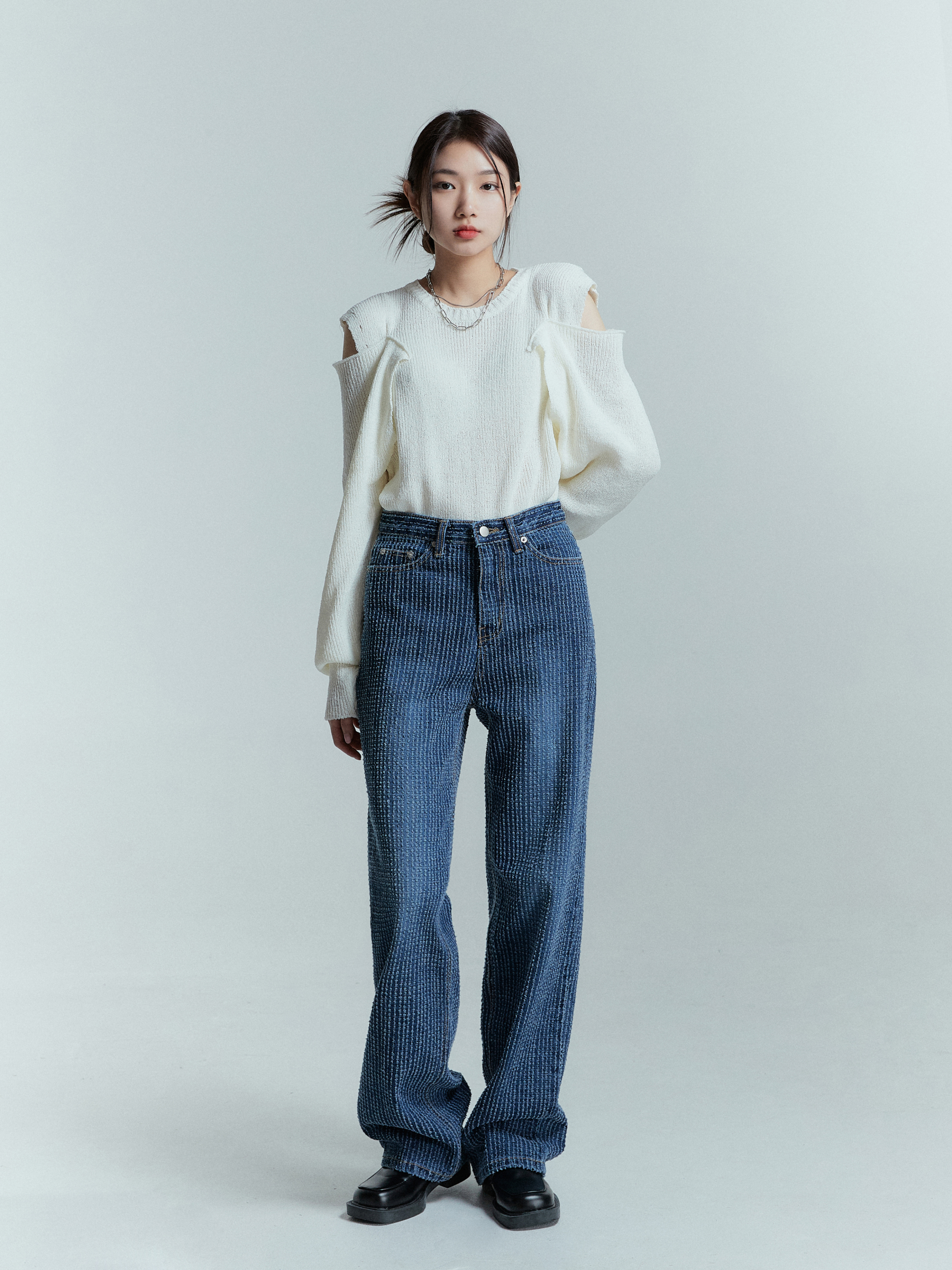 A standing pose of a model in Korean street fashion, wearing the striped jeans matched with an ivory shoulder cut sweater.