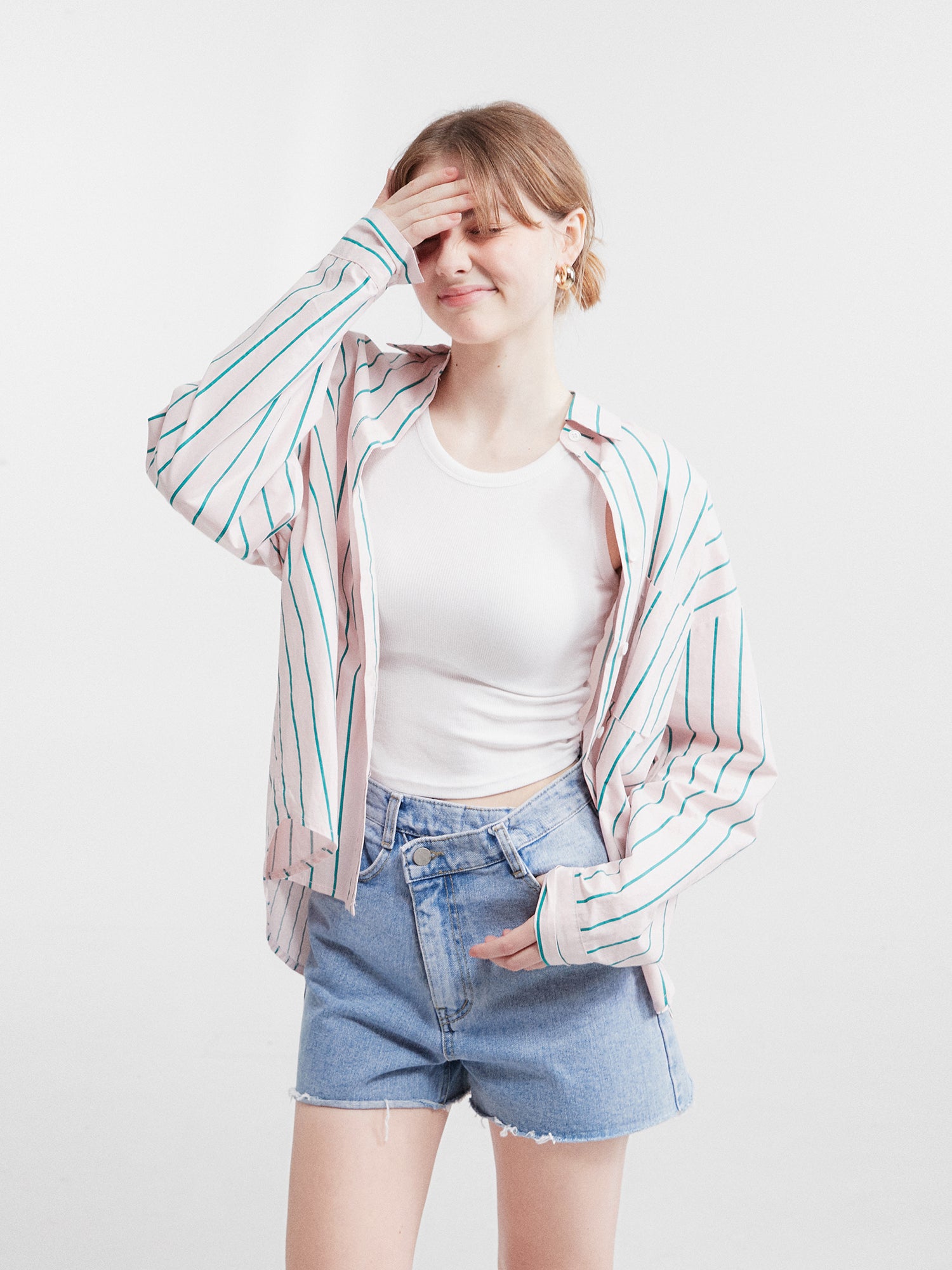 A striking front view of a model wearing the striped loose shirt, gracefully posing with her hand on her head.