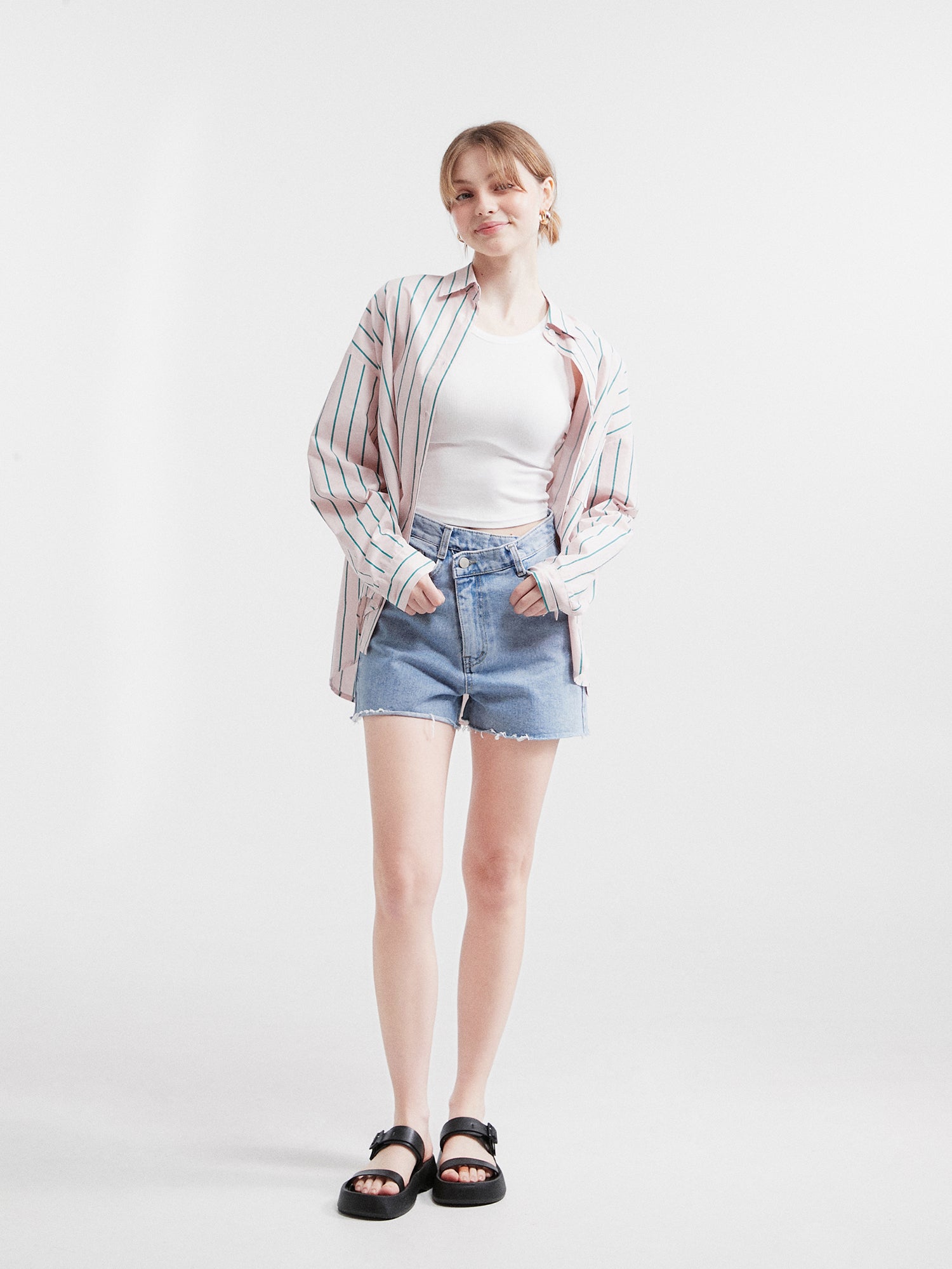 A stylish front view of a model confidently posing in the striped loose shirt, flawlessly paired with crossover jean shorts.