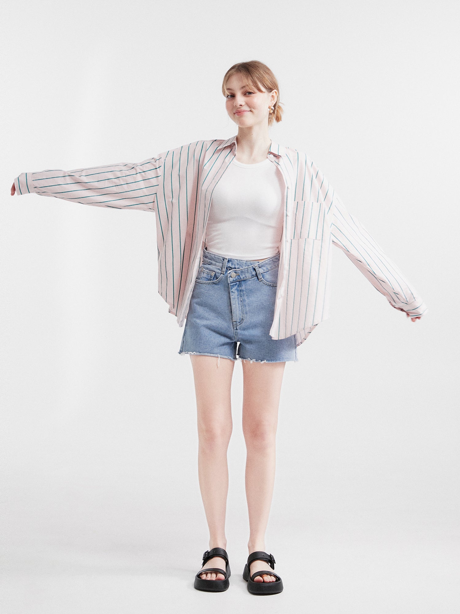 A front shot of a model gracefully posing in the striped loose shirt, showcasing its width as her arms stretch wide open.