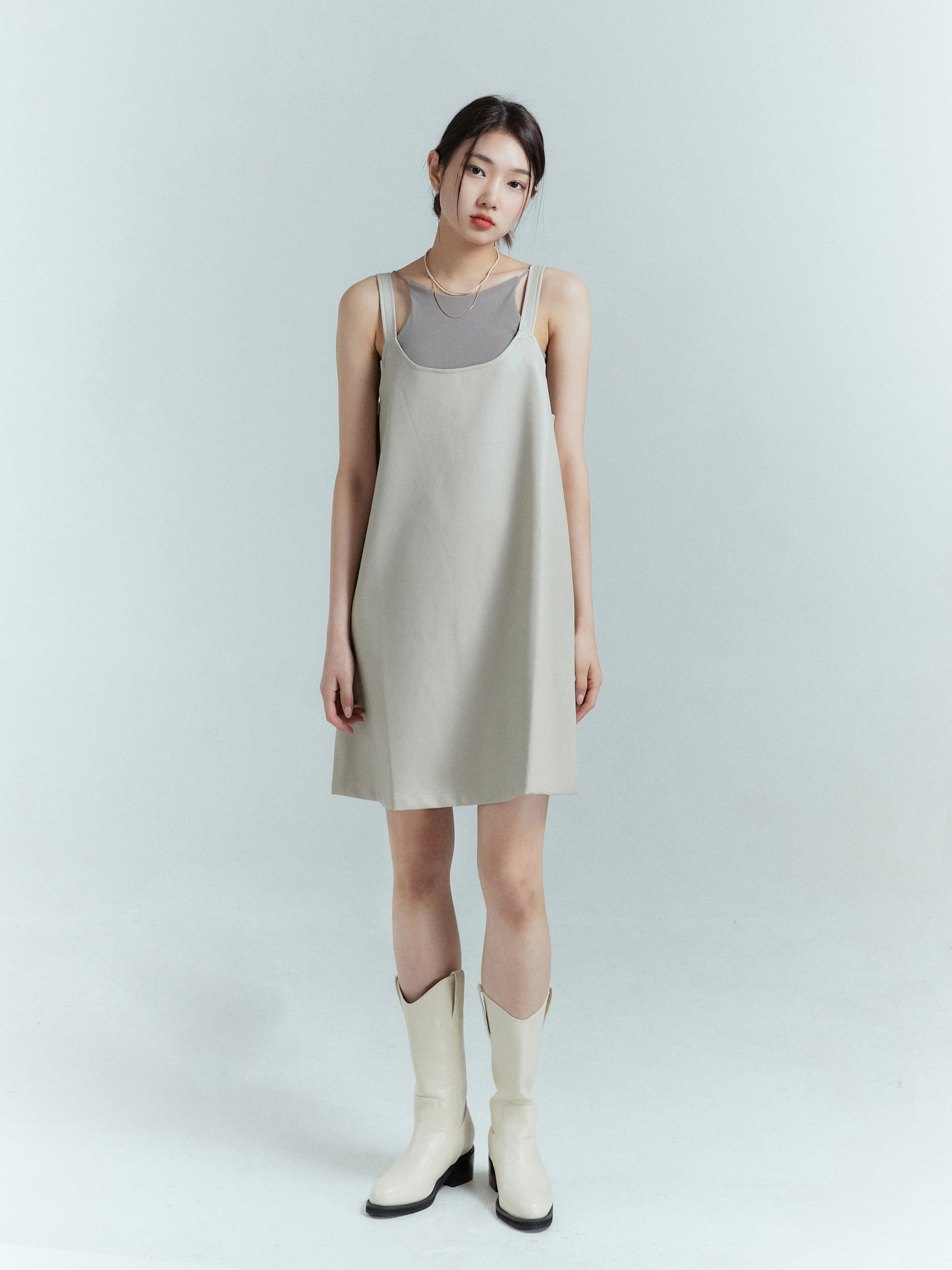 In a full-length shot, the model elegantly tilts her head, spotlighting the light beige tank dress with grace