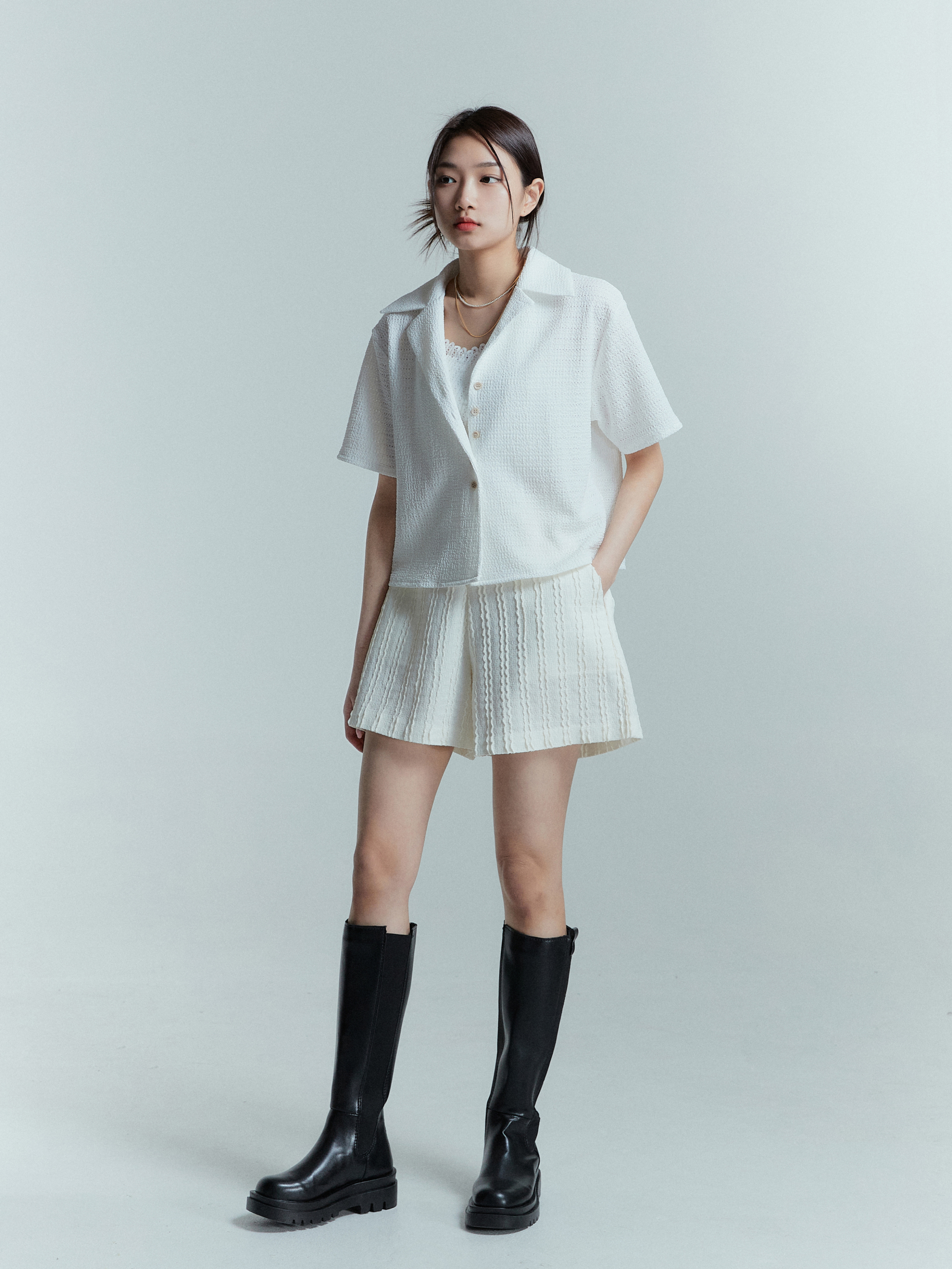 A model wearing cream textured shorts, captured from a tilted angle, with her hand casually tucked inside the pocket.