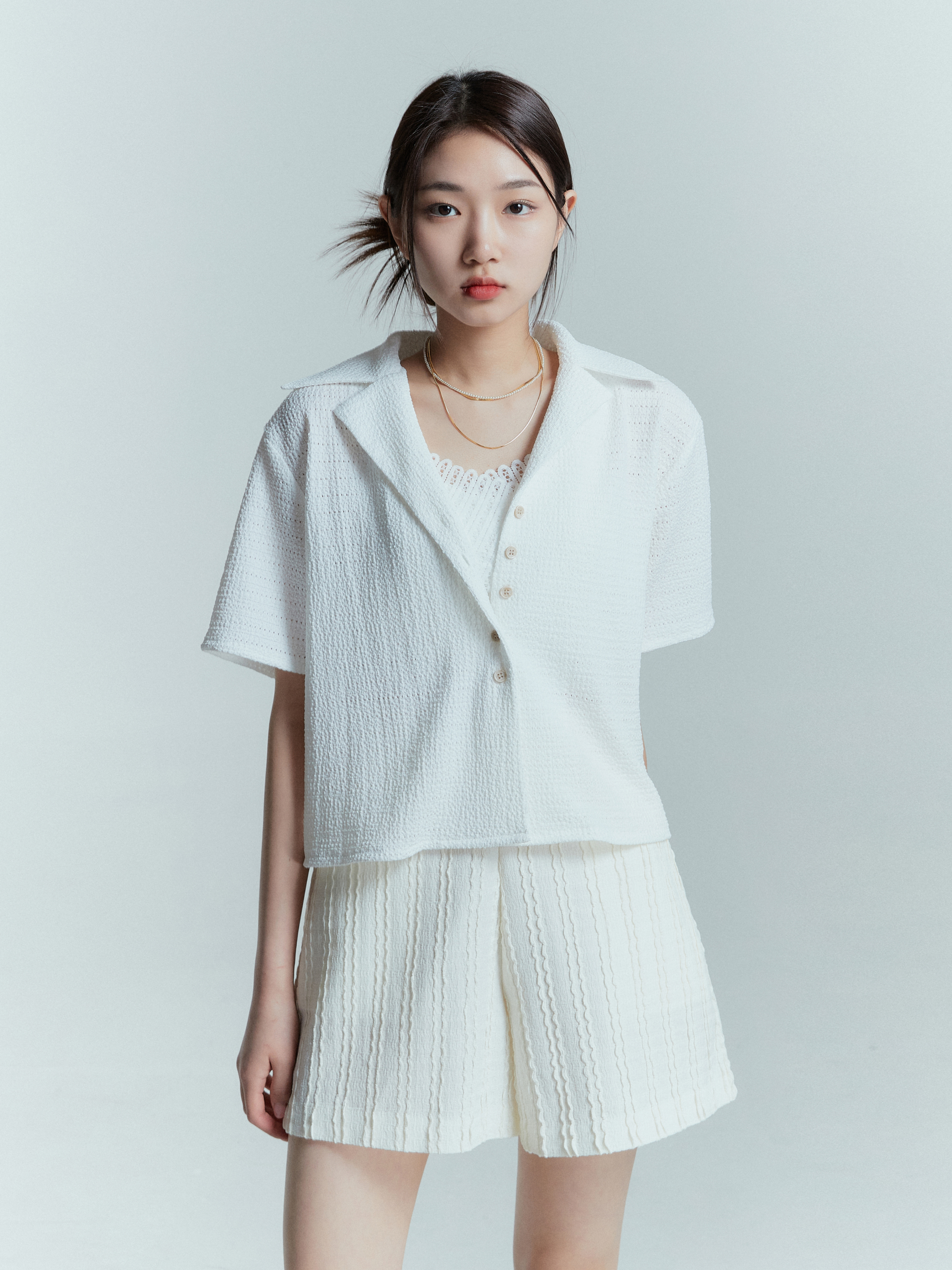 In a medium shot, a model faces the camera while wearing the textured shorts paired with collar button shirt.ng for a closer view of the intricate texture design.