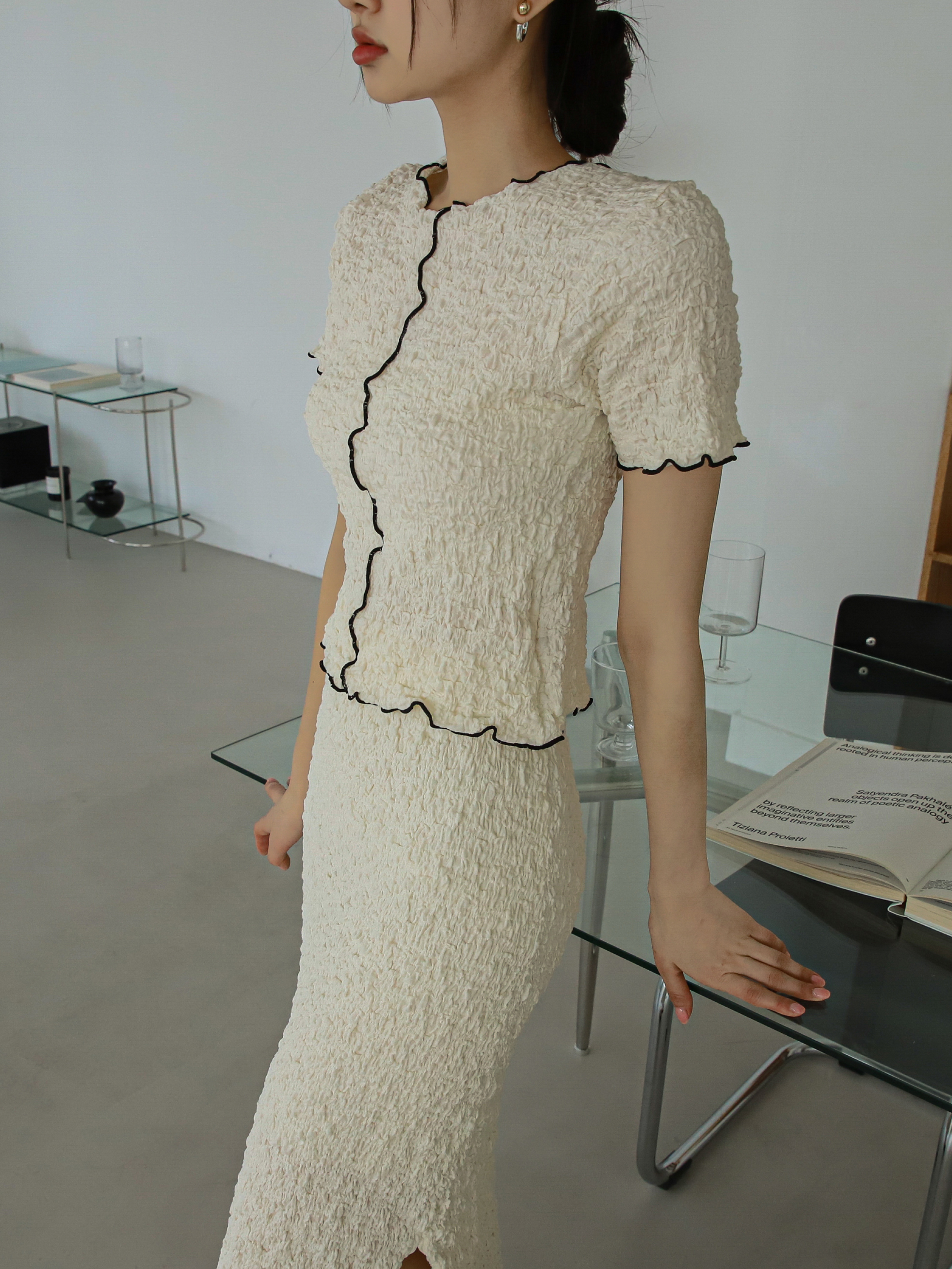 Close-up shot of a model standing against the glass table wearing the cream textured top matched with the bottom.