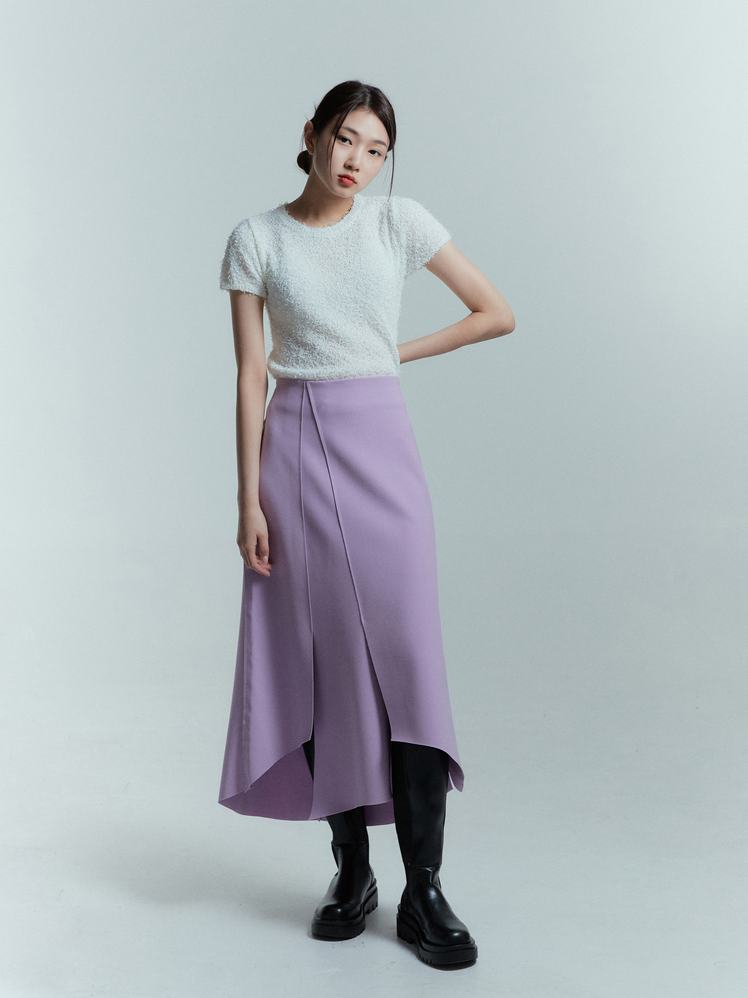 A model exudes confidence while wearing the lavender tulip wrap skirt paired with an ivory fuzzy knit top, showcasing a stylish ensemble.