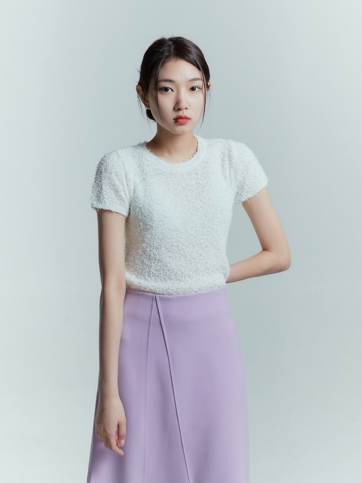 A close-up of a model wearing the tulip wrap skirt matched with ivory fuzzy knit top highlighting the intricate wrapping design detail of the skirt.