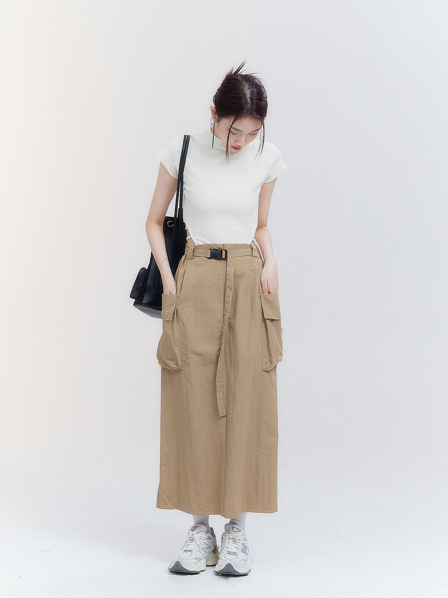 The model, with her head slightly tilted down, gazes at the cargo midi skirt, allowing a front view that reveals the intricate designs and details of the skirt.