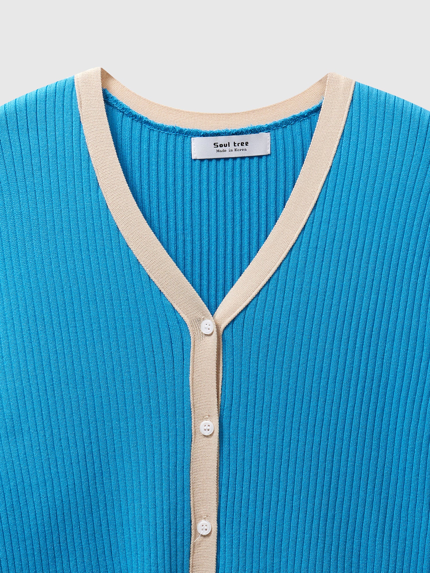 A close-up look of the blue contrasting trim cardigan highlighting the front button and the ribbed texture of the fabric.