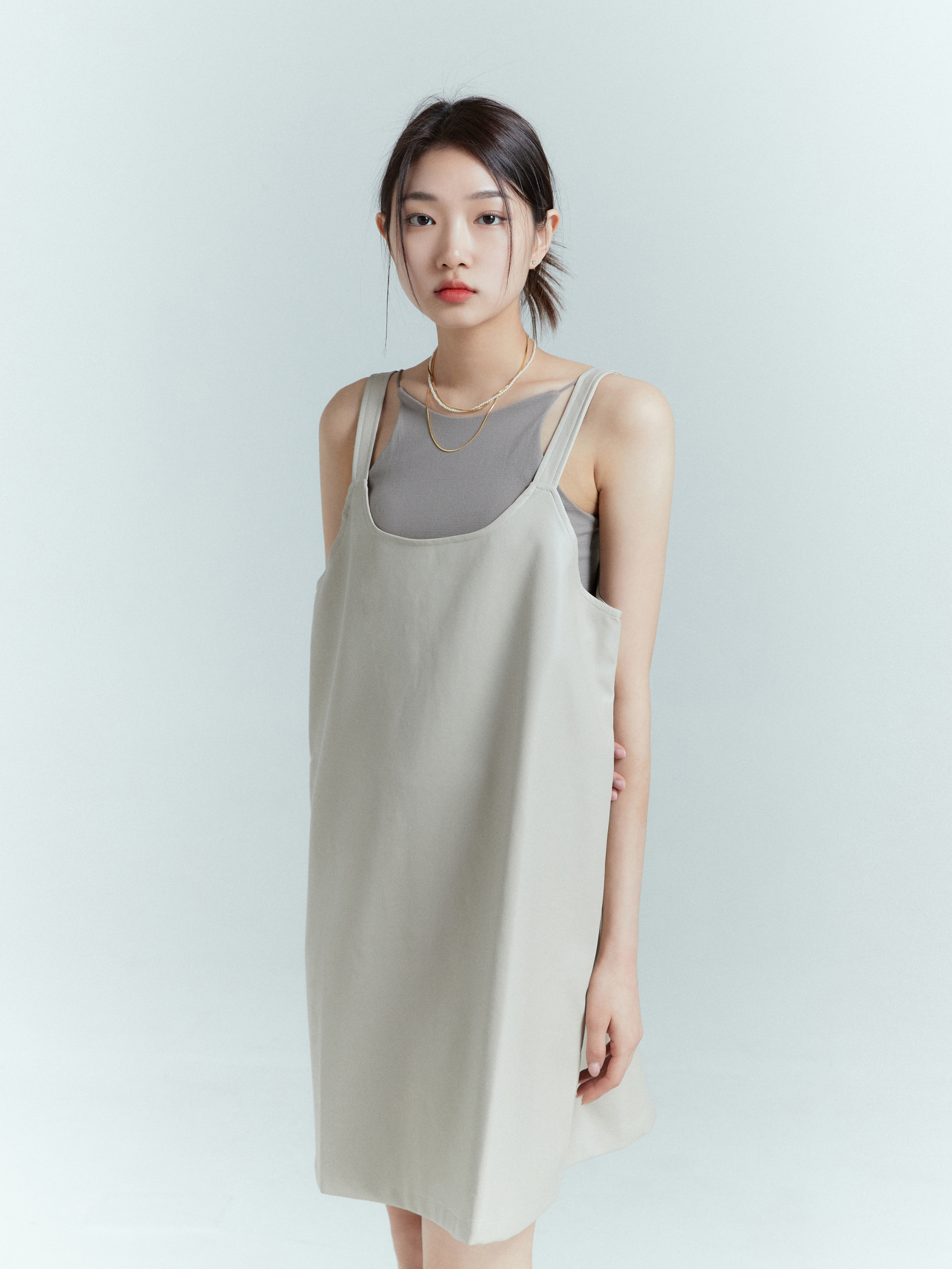 In a medium shot, showcasing contemporary fashion, the model confidently flaunts the gray spaghetti strap tank, effortlessly paired with a light beige tank dress, creating a stylish ensemble.