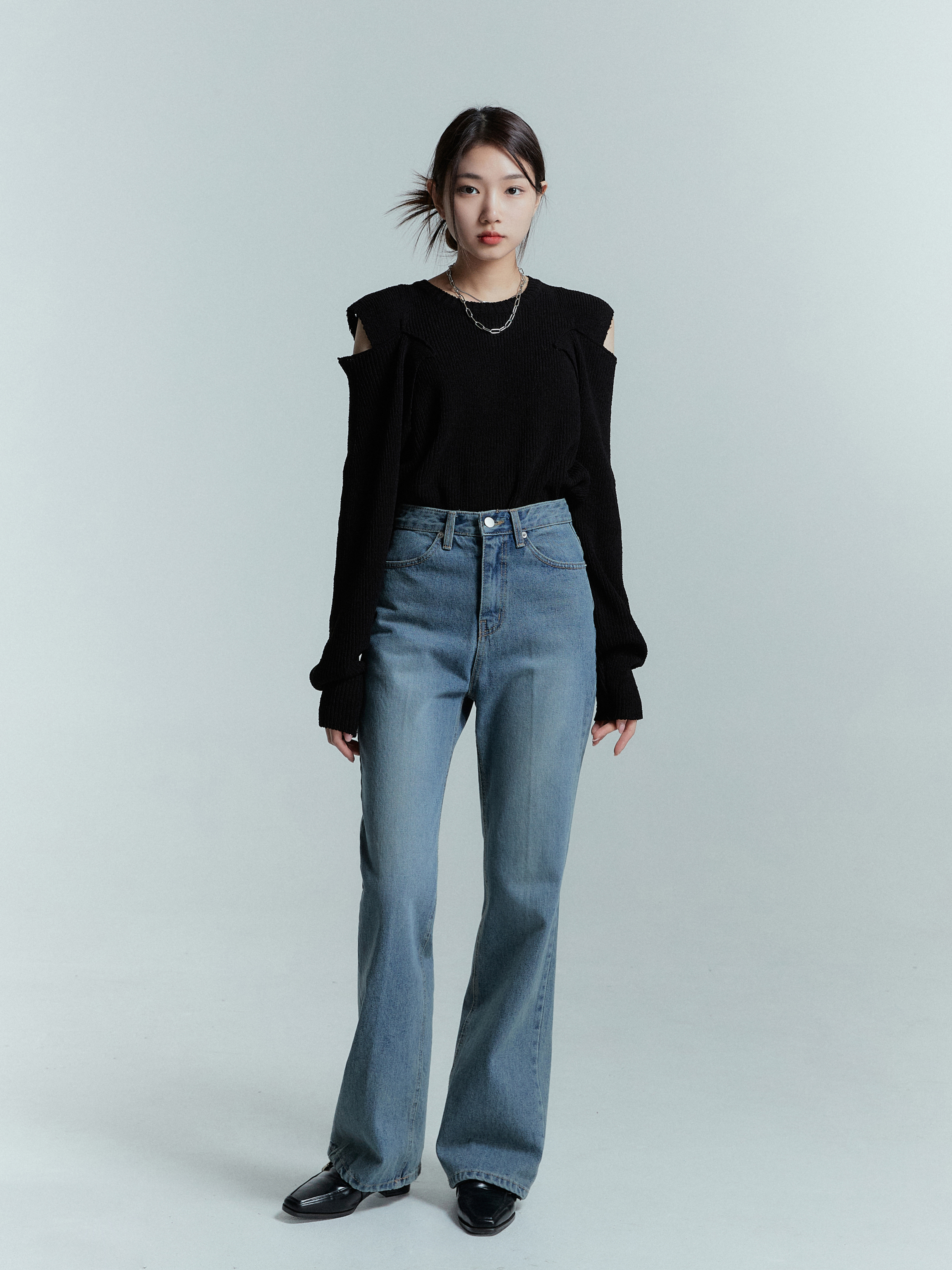 Observe the front view of a stylishly dressed model, showcasing Korean street fashion, standing confidently in wide leg jeans, flawlessly paired with a shoulder cut sweater.