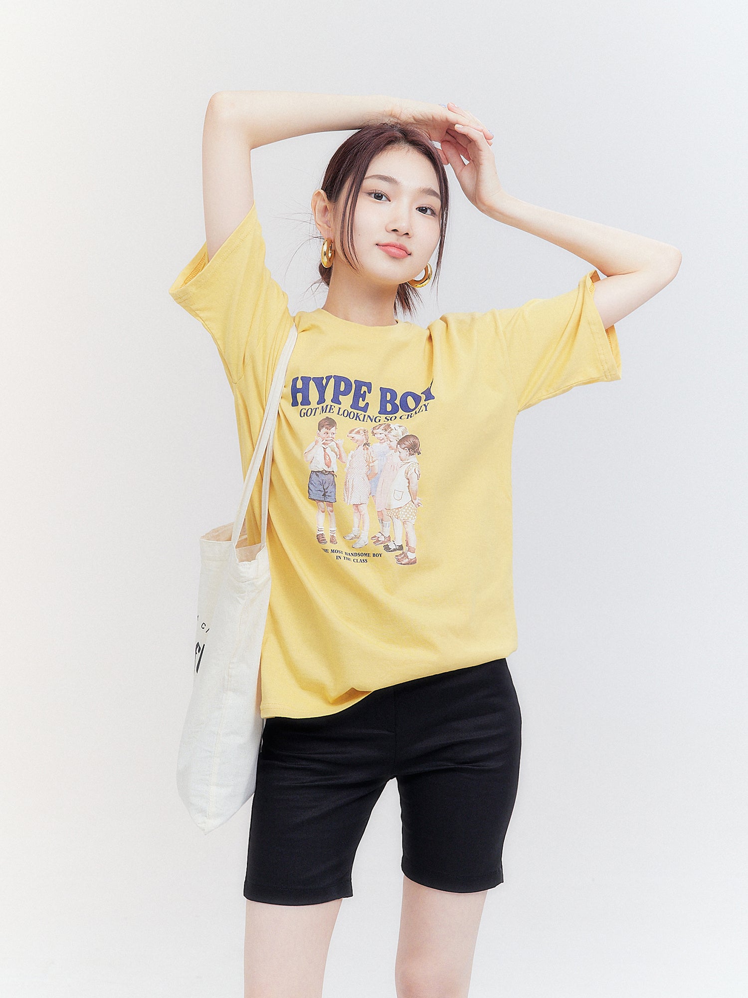 A frontal view captures the model wearing the 'Hype Boy' t-shirt, with her hands held high above her head.