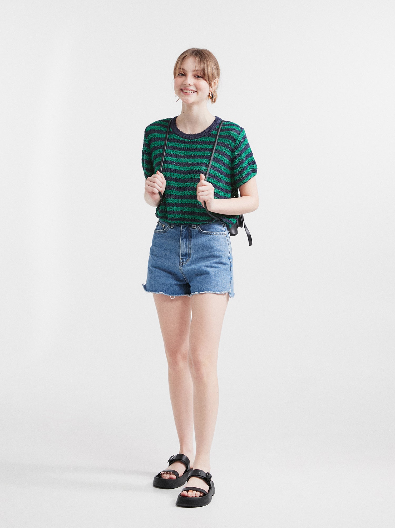 The model proudly displays Korean street style, smiling and confidently facing forward while wearing a pair of stylish jean shorts, exuding an effortless and fashionable vibe.