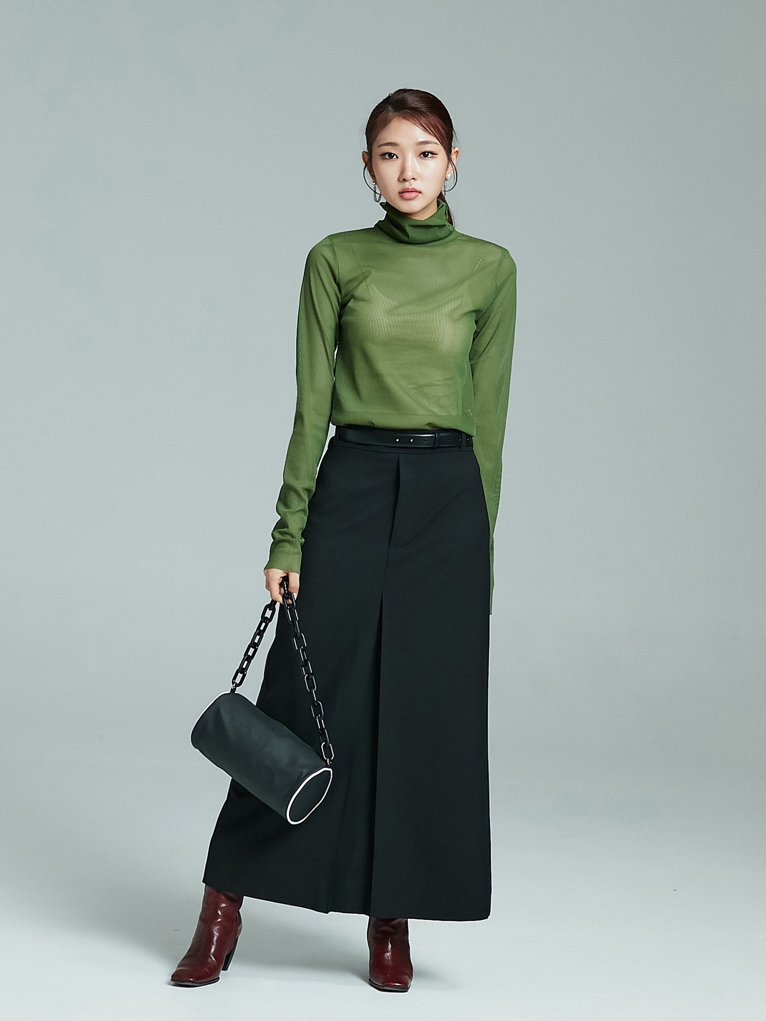 Full picture of the model wearing the green mesh turtleneck matched with front pleated maxi skirt.