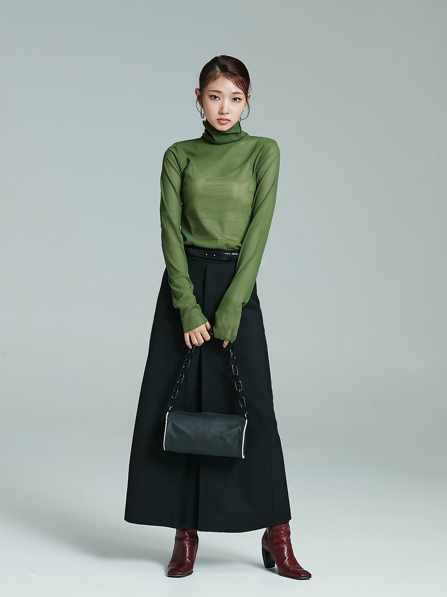 Long shot of the model wearing the green mesh turtleneck with a handbag on her hand.