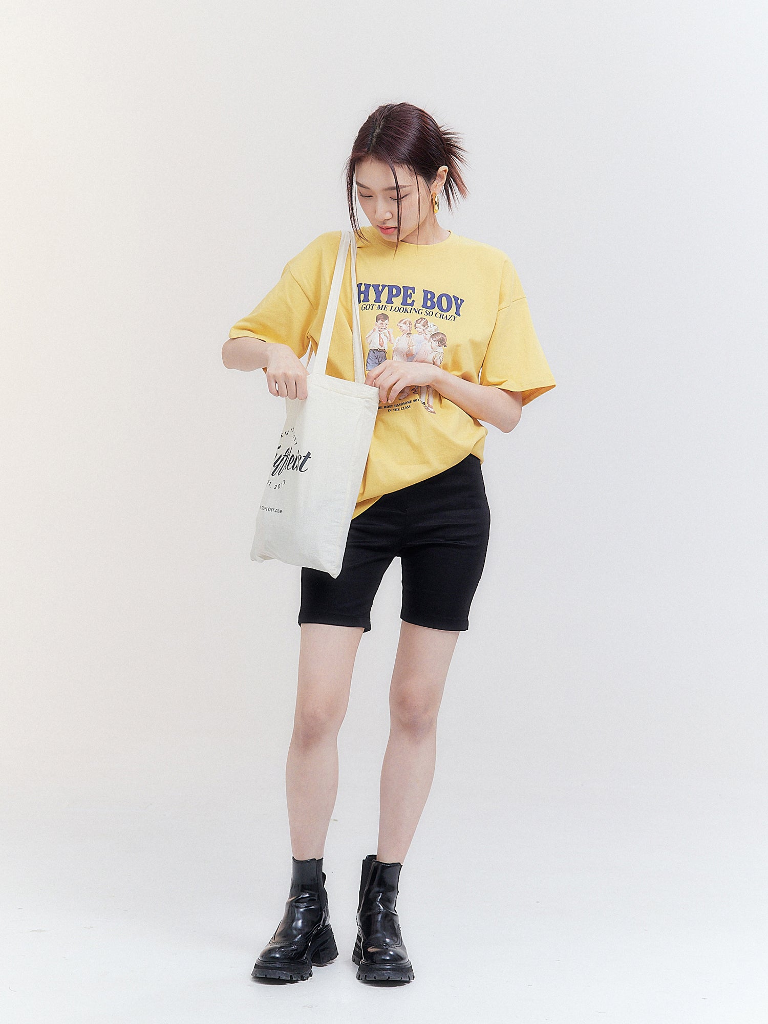 Embrace Korean street fashion as the model gazes down at her book bag, effortlessly styled with black mid-length shorts.