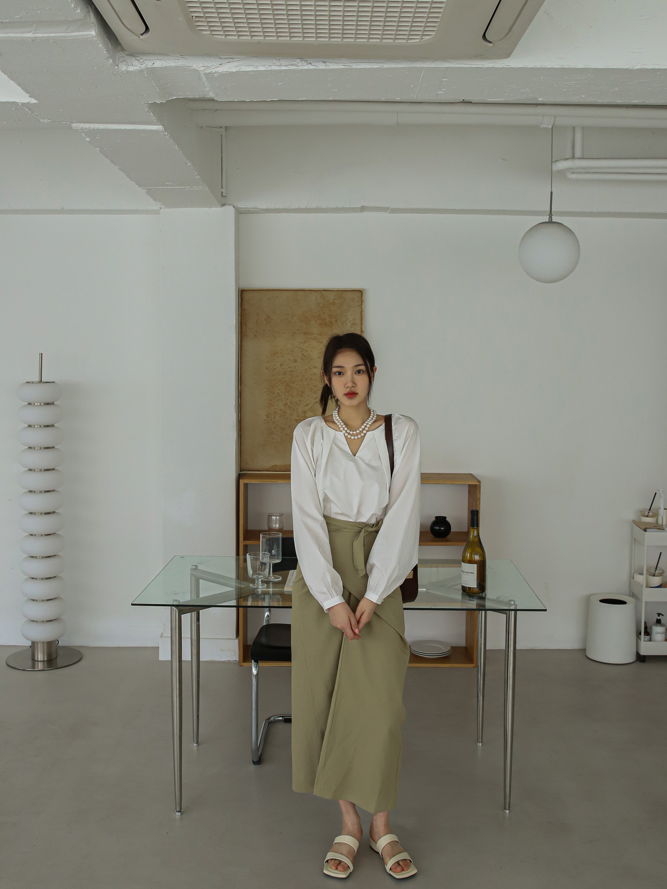 A long shot of the model looking straight wearing the ivory raglan sleeve blouse matched with the beige wrap midi skirt.