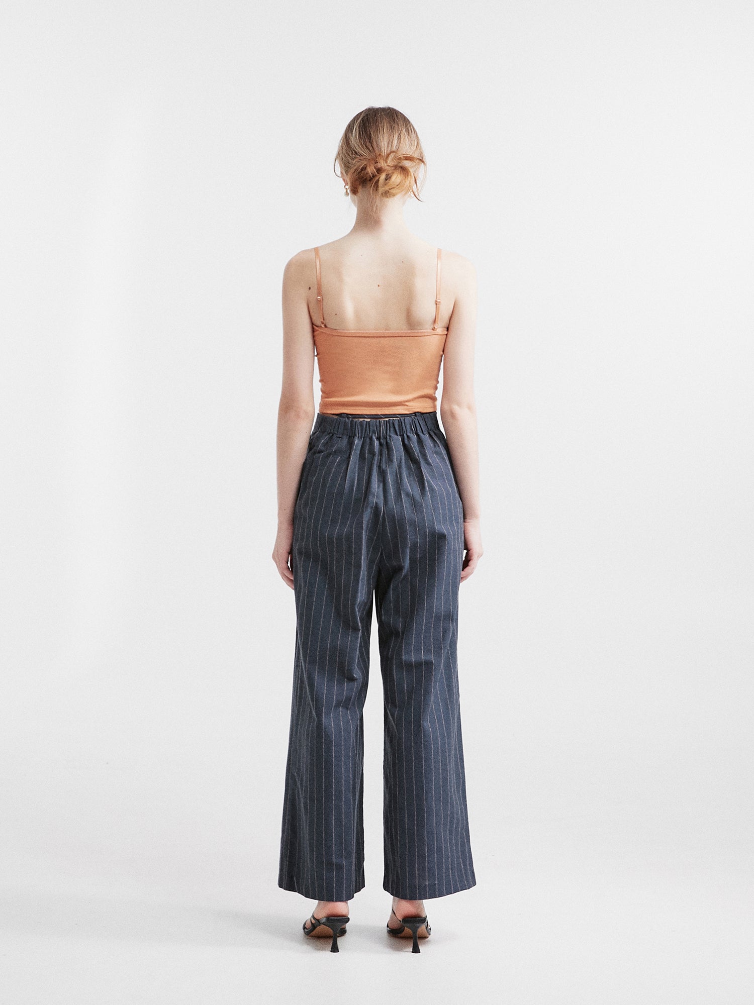 A back view of the model wearing the striped belt-tie trouser showcasing back side of the trouser.