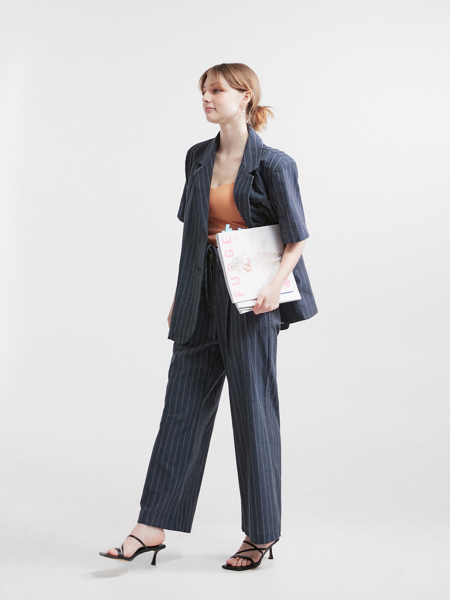 A side-angle view capturing contemporary fashion, as the model elegantly showcases the striped belt-tie trouser, highlighting the intricate details and silhouette of the garment from a different perspective.