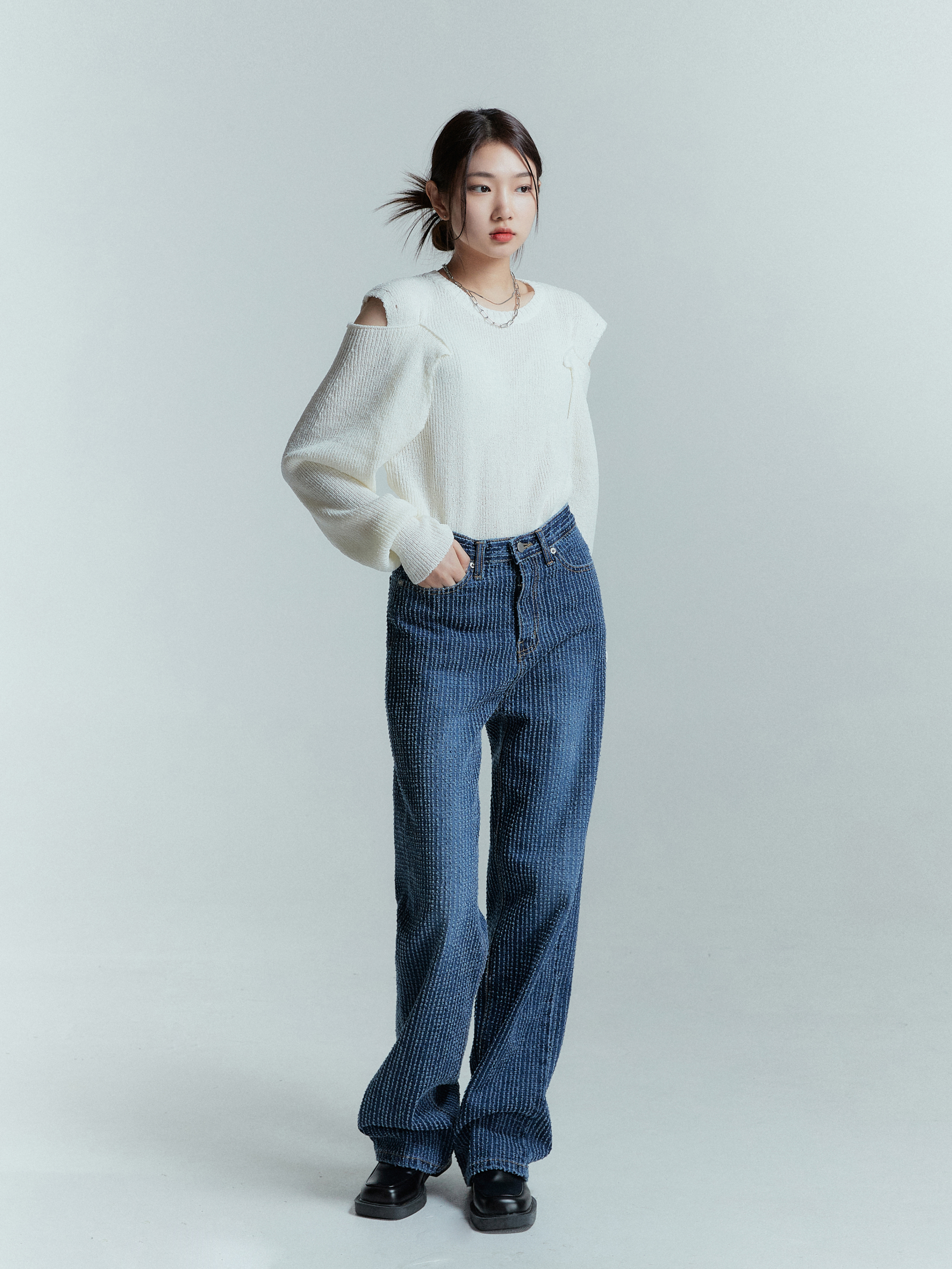 The model strikes a pose, showcasing the striped jeans paired with an ivory shoulder-cut sweater, exuding effortless style.