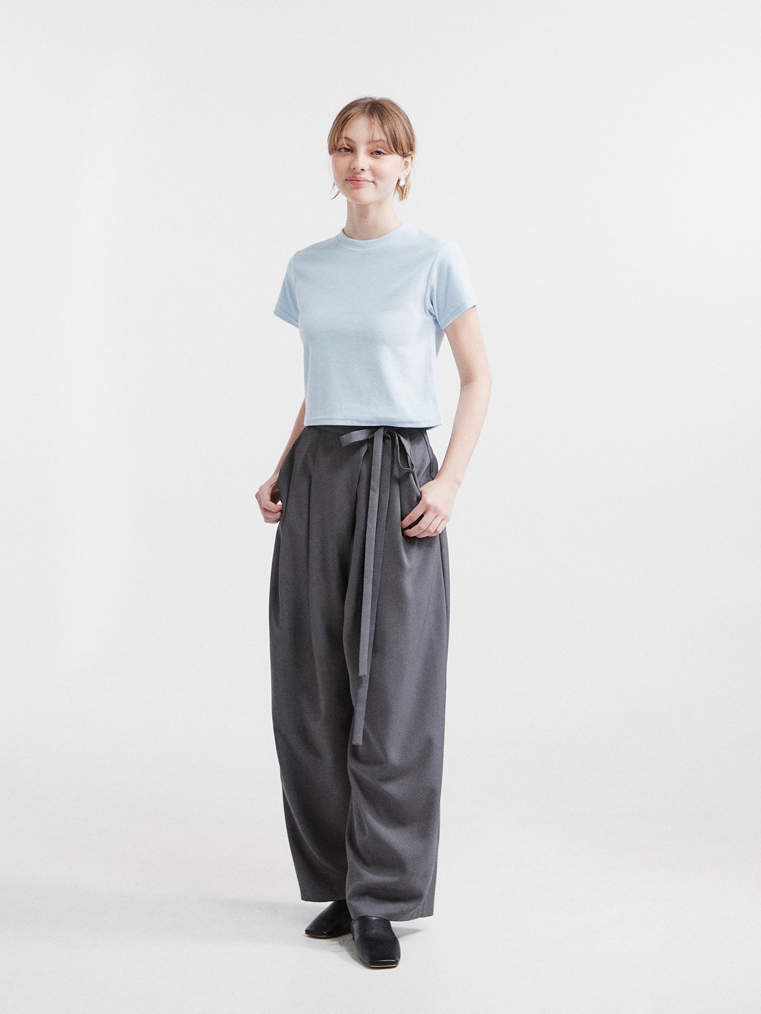 A standing shot of a model wearing the crewneck top matching it with the side-belted trouser.