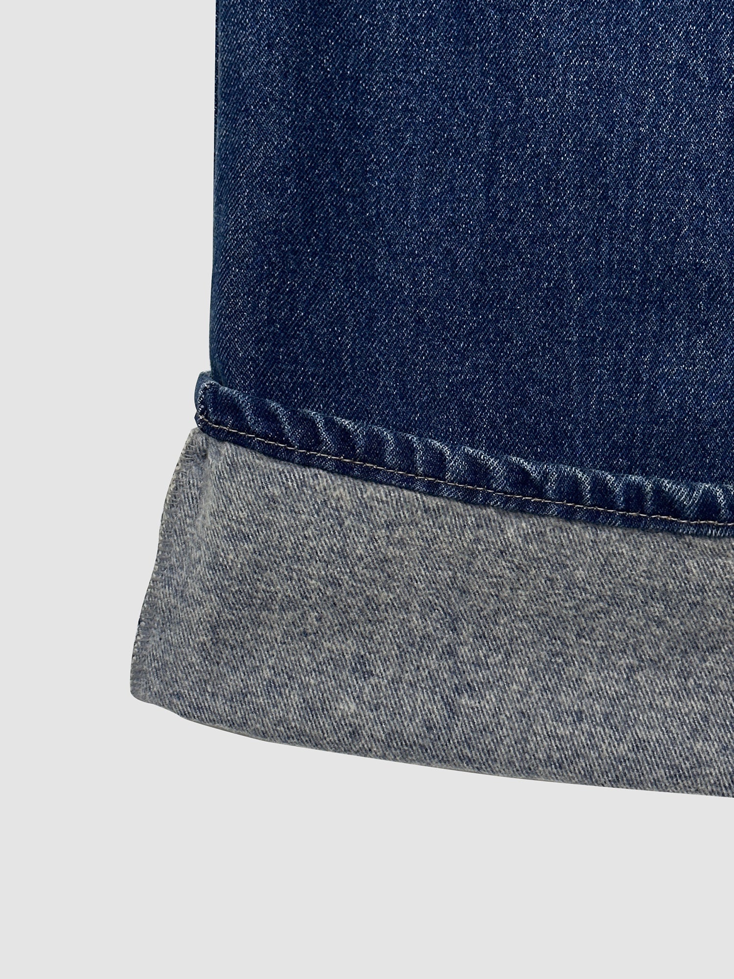 A close-up examination of the denim jeans, featuring the folded bottom to highlight the intricate stitching details.