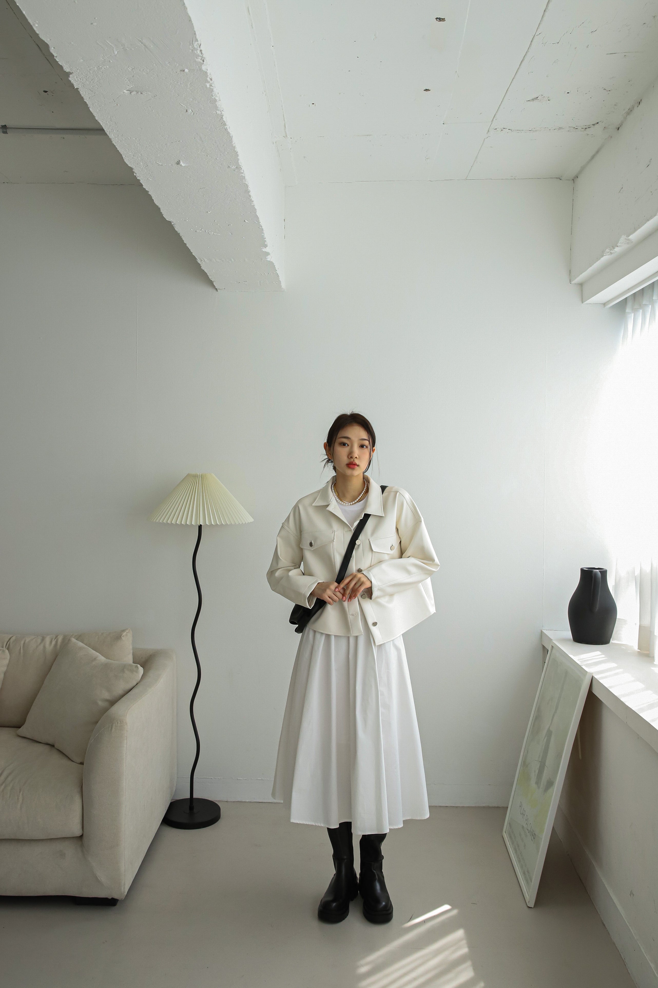 A full-shot of the model wearing white leather jacket matching it with white midi dress.